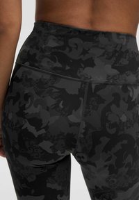 Korkeavyölastiset mustat legginsit, joissa on hienovarainen mattapinta ja monimutkainen tumma kuvio, jossa on kukka- ja pitsimäisiä yksityiskohtia. Sujuva pinta.