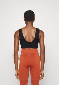 Sutiã desportivo preto com um design de costas baixas, combinado com leggings laranjas de cintura alta apresentando riscas diagonais embutidas e detalhe do logo.