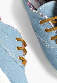 Scarpe da tennis blu chiaro in tela con lacci marroni, foderate in tessuto scozzese, suole di gomma bianche e dettagli di cucitura visibili.