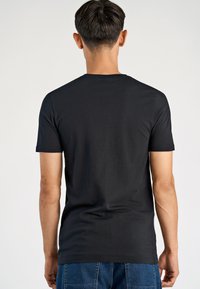 T-shirt nera a maniche corte con scollo rotondo, texture liscia e silhouette aderente, mostrata di spalle su uno sfondo neutro.