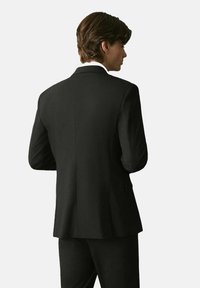 Giacca nera con un taglio sartoriale, rever a punta e una texture liscia. Presenta un design pulito e minimalista con una sola apertura.