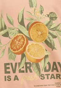 Lichtroze stof met een ontwerp van sinaasappel- en citroenschijven omringd door groene bladeren. De tekst luidt: "IEDERE DAG IS EEN VERS BEGIN."