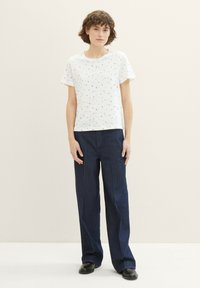 T-shirt blanc à manches courtes avec un motif coloré, associé à un jean large bleu foncé. Tissu lisse et coupe décontractée.