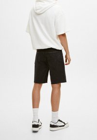 Bermudas de mezclilla negras con dobladillos deshilachados, combinadas con una sudadera blanca y zapatillas en blanco y negro. Las características de diseño visibles incluyen bolsillos traseros.