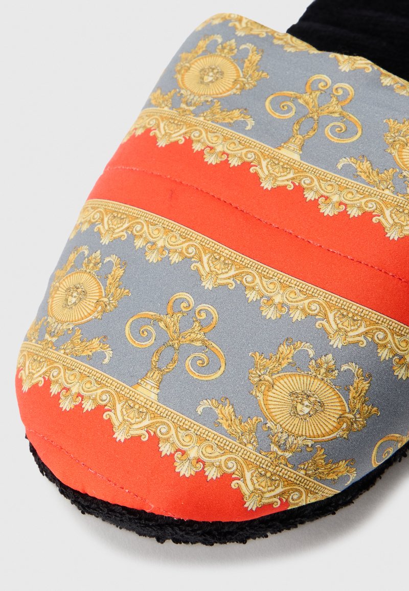 Gepolsterte Hausschuhe mit einem grau-orangen Design, verziert mit goldenen, opulenten Mustern und Texturen, ergänzt durch ein schwarzes Fleece-Futter.