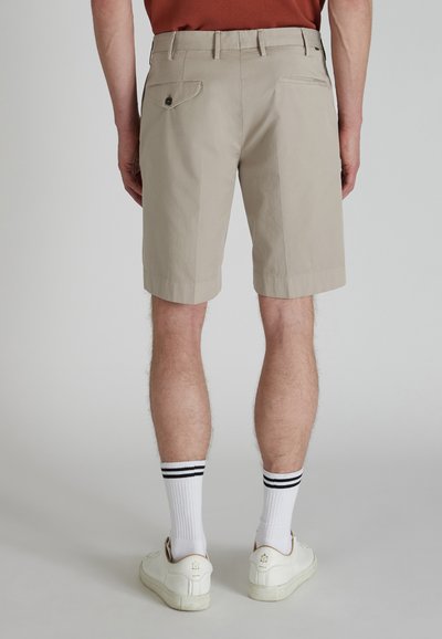 Pantaloni corti beige in tessuto morbido, di lunghezza al ginocchio con una texture liscia. Presenta due tasche posteriori, una con chiusura a bottone, indossati con calzini bianchi e sneaker.