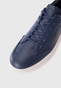 Baskets en cuir bleu marine à finition texturée, avec des lacets plats, un bout arrondi et une semelle en caoutchouc blanche. Design minimaliste avec des accents lisses.