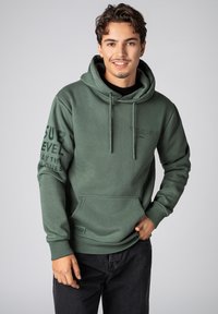 Groene hoodie met een voorzak, verstelbare trekkoorden en bedrukte tekst op de mouw. Heeft een zachte textuur en een ontspannen pasvorm.
