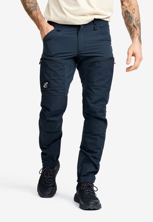 Marina stretchbyxor med dragkedjefickor, smal passform, förstärkta knän och kontrasterande sömmar. Materialet är slitstarkt och har en jämn textur.