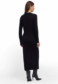 Czarna dzianinowa sukienka z długim rękawem o dopasowanym fasonie, sięgająca do połowy łydki. Połączona z czarnymi, sięgającymi do kolan, szpilkami o gładkiej fakturze.