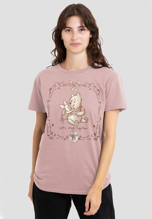 Young woman wearing a pink t-shirt with Winnie the Pooh hugging Piglet and the text "Let's stick together" framed by floral design.