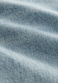 Lichtblau denim stof met een kenmerkende twill-weving; zichtbare textuur en een zachte oppervlakte creëren een gelaagd, rimpelig uiterlijk.