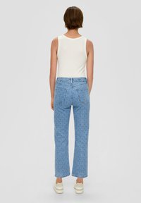 Jean en denim bleu clair avec un motif en forme de coquille, coupe droite et poches arrière. Assorti avec un débardeur blanc et des chaussures claires.