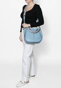 Borsa a tracolla in pelle blu chiaro con un design curvo, dotata di una tracolla a righe e dettagli in metallo dorato. Texture liscia con dettagli di cucitura.