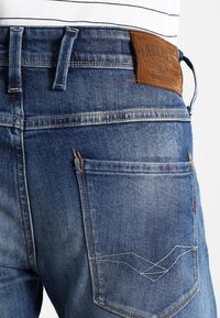 Mörkblå denimjeans med en läderlapp i midjan, kontrasterande sömmar och en bakficka med zickzack-sömnadsdetalj.