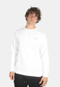 Felpa bianca con maniche lunghe, polsini e orlo a costine, con un piccolo logo grigio sul lato sinistro del petto. Tessuto liscio.