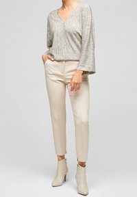 Light gray, textured v-neck sweater with wide sleeves, paired with beige tailored pants and cream ankle boots with zippers.