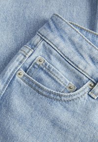 Svijetloplave traperice s jednim prednjim džepom s srebrnim zakovicama, teksturirana tkanina i kontrastni šavovi duž rubova.