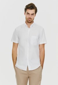 Krótki rękaw biały, zapinany na guziki shirt z kieszonką na piersi, gładka faktura i klasyczny kołnierzyk, w połączeniu z jasnobeżowymi spodniami.