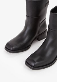 Para czarnych skórzanych botków za kostkę z kwadratowymi noskami i niskimi obcasami na białym tle.