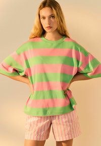 Camisa de manga corta de gran tamaño a rayas verdes y rosas, combinada con pantalones cortos a rayas rosas y blancas, confeccionados en una tela suave.