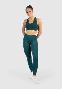 Turkusowy stanik sportowy i legginsy z wysokim stanem wykonane z elastycznego materiału. Legginsy mają delikatne wzory tekstowe i gładką fakturę.