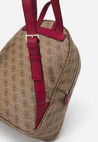 Bolso de mano de tela marrón con un diseño estampado, asas texturizadas rojas, herrajes dorados y cierre de cremallera en el lateral. Forma curvada.