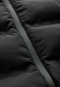 Gros plan sur un tissu de doudoune noire avec une fermeture éclair centrale visible et des sections matelassées cousues.