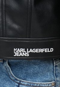 Mustad nahast teksad, millel on topstitšitud detailid ja vöökoht, millel on silmapaistvalt valge "KARL LAGERFELD JEANS" logo.