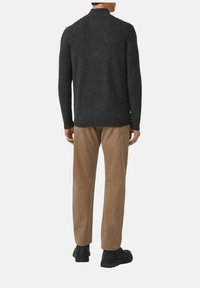 Maglione a maglia grigio scuro con collo alto, indossato con pantaloni marrone chiaro a gamba dritta e scarpe nere. Tessuto morbido, design minimalista.