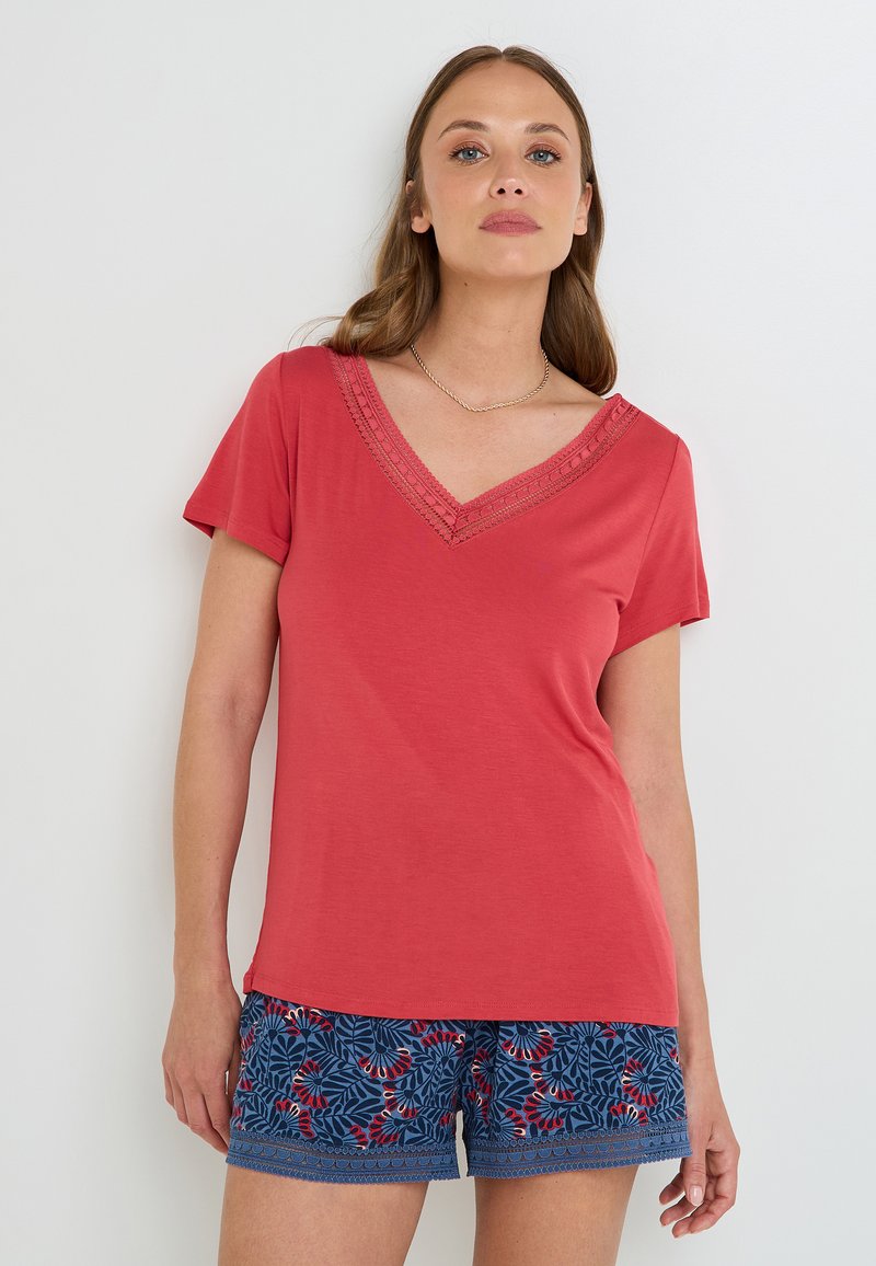 T-shirt à col en V en corail avec des manches courtes, ornée de dentelle. Associé à un short bleu à motifs avec des accents floraux rouges.