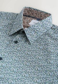 Chemise à boutons à imprimé floral bleu avec col ouvert présentant une doublure intérieure contrastante à imprimé floral rouge et blanc.