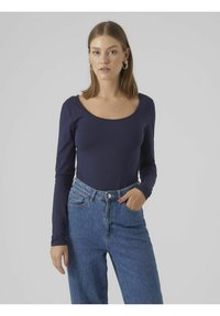 Marineblaues Langarmshirt mit Rundhalsausschnitt, kombiniert mit hochgeschnittenen blauen Jeans. Glatte Stofftextur, taillierte Passform.