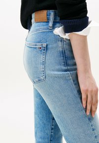 Jeans in denim azzurro chiaro con vita alta, caratterizzati da una patch in pelle marrone con logo, dettagli sulle tasche posteriori e una vestibilità slim.