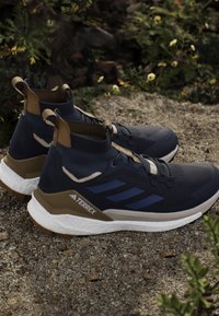 Marinefarbene Wanderschuhe mit einem hohen Knöcheldesign, ausgestattet mit braunen Akzenten, strukturiertem Stoff, weißer Zwischensohle und schwarzem Gummiaußensohle.