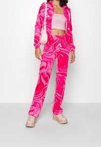 Rosa, marmor-mönstrad träningsdräkt i mjukt material, med en zip-up jacka och byxor med dragsnöre. Kommer med kraftiga beigea sneakers.