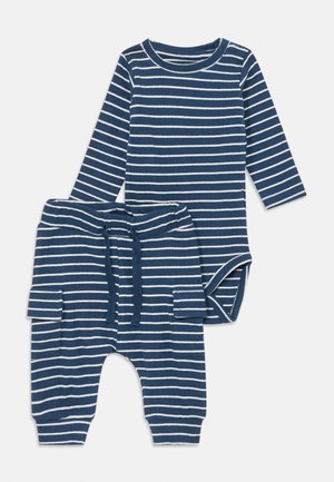 Prugasta bebaška odjeća koja se sastoji od bodija s dugim rukavima i odgovarajućih hlača. Izrađena od mekog pamuka u tamnoplavoj boji s bijelim prugama, uključuje vezicu i džepove.