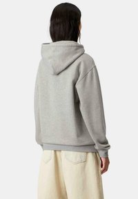 Sudadera con capucha gris de corte relajado, que presenta una textura suave y puños acanalados. Combinada con pantalones de pierna ancha de color claro.