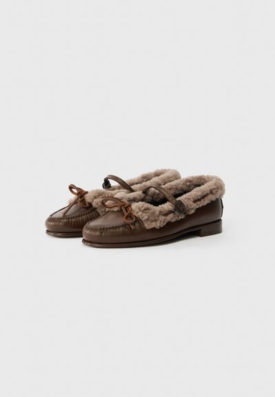 Brown leather slippers with a fuzzy beige lining, featuring a rounded toe, small heel, and decorative loops on the front.