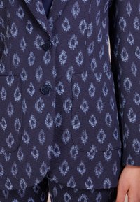 Navy-mönstrad blazer med strukturerat tyg, blå diamantformer, två framfickor och blå knappar. Skräddarsydd passform med slag.