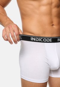 Hvide boxer shorts med et sort elastisk bælte med "INDICODE" i grå skrift. Blødt materiale, tætsiddende pasform og glat struktur.