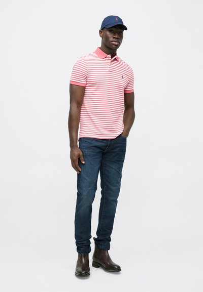 Pruhované červenobílé polotriko s růžovým límečkem, tmavě modré džíny a hnědé kotníkové boty. Součástí je také tmavě modrá čepice s logem.