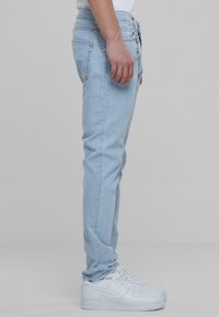 Jeans de denim azul claro con un corte ajustado, que presentan un detalle de cadena en la cintura, combinados con zapatillas blancas. Textura suave, con un desgaste mínimo.
