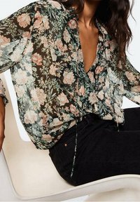 Blusa floreale in tessuto nero trasparente con fiori pastello. Vestibilità rilassata, scollo a V e dettagli legati sul davanti. Abbinata a jeans scuri.