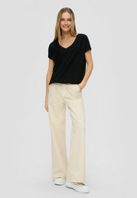 Zwarte korte mouw V-hals top gecombineerd met beige wijde broekspijpen. De outfit wordt aangevuld met witte sneakers. Gelaagde stof van de top is zichtbaar.