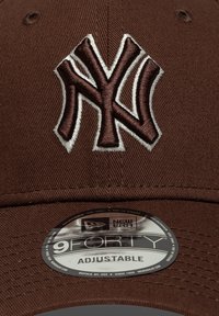Καφέ καπελάκι με αυξομειούμενο μέγεθος, που διαθέτει έντονο κεντημένο λογότυπο 'NY' σε καφέ και λευκό χρώμα. Περιλαμβάνει στρογγυλή ετικέτα «9FORTY» στο γείσο.
