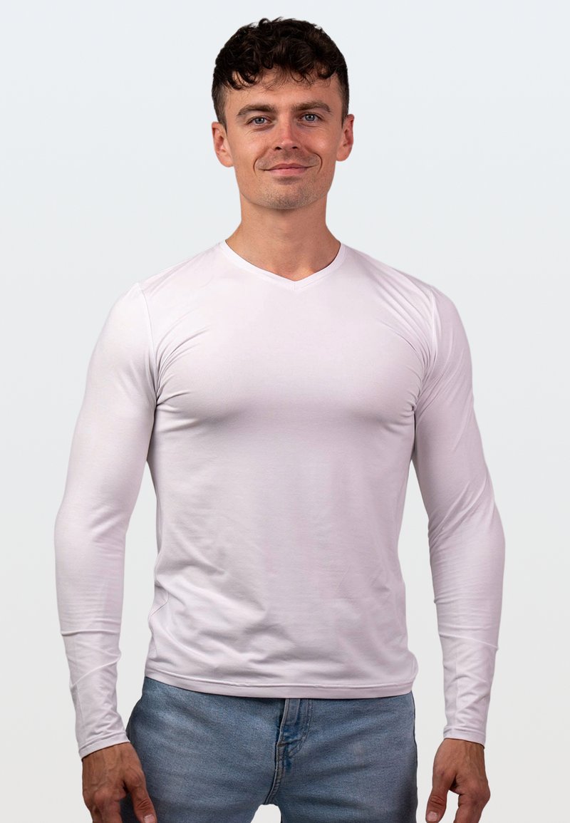 Biała, długa koszulka z długim rękawem w serek, wykonana z gładkiego materiału, dopasowany krój, noszona z jasnoniebieskimi dżinsami. Minimalistyczny styl.