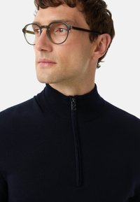Marineblauer Zip-Kragen-Pullover mit strukturiertem Finish und hohem Kragen. Verfügt über einen halben Reißverschluss und gerippte Bündchen. Das Material wirkt weich und leicht.