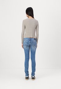 Camiseta de manga larga a rayas con cuello redondo y dobladillo dividido, combinada con jeans skinny de denim azul claro que cuentan con bolsillos traseros y detalles de costura.