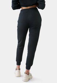 Zwarte joggingbroek van zachte stof, met een elastische tailleband, aansluitende enkels en zijzakken, gecombineerd met witte sneakers.